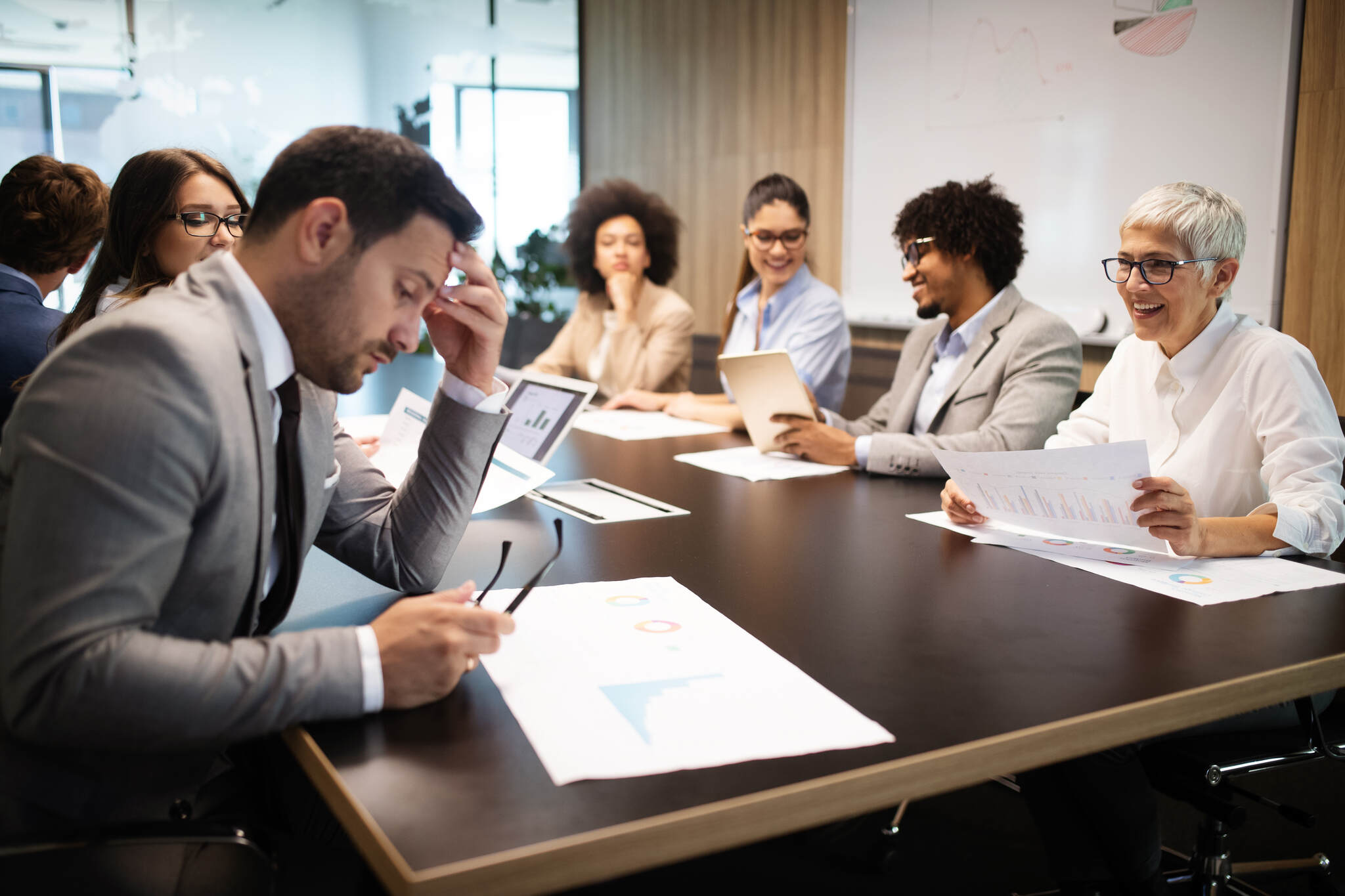 Team of professionals reviewing EU funding application documents during a meeting, with one visibly stressed man highlighting the impact of common mistakes in EU funding applications.